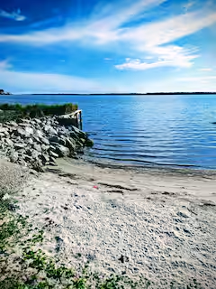 A sandy and rocky shoreline beside blue coastal water